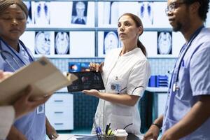 Diverse doctors team looking at radiography scan test result to check organs condition, examining liver and lungs to fight illness. Group of physicians discussing healthcare services for wellness. photo