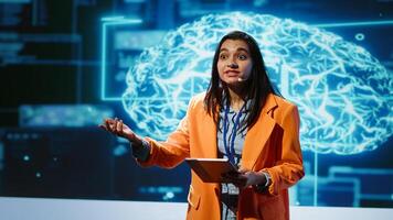 Tech startup leader using convention as platform to offer latest AI services. Businesswoman holding tablet uses microphone to talk with investors interested in artificial intelligence, camera A photo