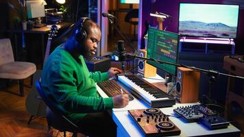 Talented famous composer writes down new verses and lyrics in home studio, composing music with digital software. Artist songwriter works with audio equipment and gear, recording tracks. Camera B. photo
