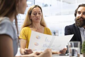 Consultant discussing with women, presenting informational materials and recommending ideal insurance policies. Agent teaching clients of investment options, showing them statistics charts photo