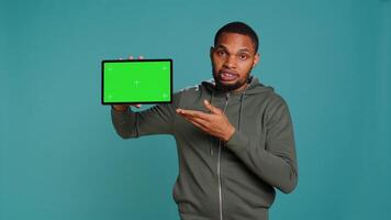 Tech content creator holding isolated screen tablet, doing promotion, talking with audience. Man pointing towards chroma key digital device, doing advertising, studio backdrop, camera B photo