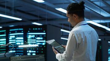 System administrator overseeing data center, making improvements and updates to ensure system can handle networking tasks. IT expert in server room tracking network traffic with tablet, camera A photo