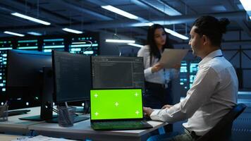 Data center engineer responsible for installation of networking equipment solving tasks on isolated screen laptop. Man doing maintenance on server room infrastructure using mockup notebook, camera B photo