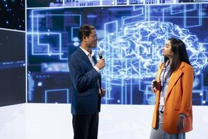 Speaker interviewing guest during presentation, exploring ways emerging AI technologies can enhance businesses. IT company colleagues at event present artificial intelligence tech photo