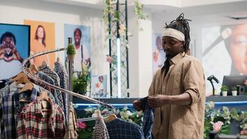 Man closely looking at shirts in clothing store, trying to determine if materials are qualitative. Customer analyzing garments in fashion boutique, looking to buy only top quality resistant apparel photo
