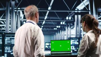 Certified IT programmers looking around high tech data center, using green screen laptop to crosscheck disaster recovery plan and assess server systems in need of replacement, preventing failures photo