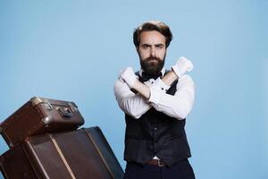 Bellboy presents rejection sign with arms, being displeased and creating stop symbol on camera. Hotel porter employee showing refusal and dismissing something, declining ideas. photo