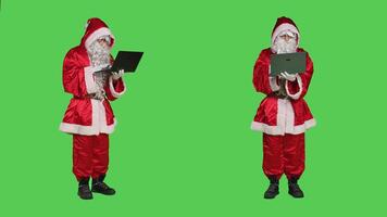 Santa claus cosplay works with laptop over greenscreen full body backdrop, using online browser in studio. Father christmas searching internet site while he is dressed with costume and hat. photo