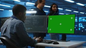 IT technician looking at green screen PC, working in data center, ensuring optimal performance. Man monitoring energy consumption across operational server rigs components using chroma key monitor photo