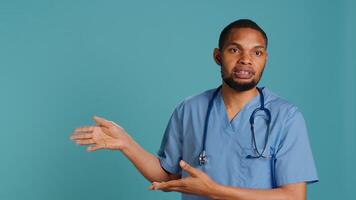 Portrait of african american nurse pointing hands towards empty space, doing advertising, talking with audience. Healthcare employee doing promotional ad, showing copy text, studio backdrop, camera A photo