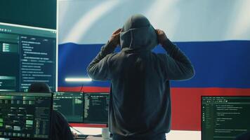 Russian hacker with a hood installing panic by misconception and manipulation, working in governmental cyber operations room. Impact of fake news and ideology propaganda in a hybrid war. Camera A. photo