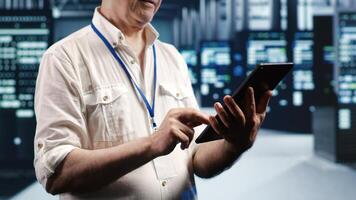 Tech savvy professional navigating network of server rigs in industrial cloud computing company. Manager with tablet doing assessments and optimizations in data center, preventing system pitfalls photo
