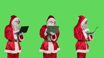 Cool santa claus character with laptop, checking xmas naughty or nice list of children against greenscreen backdrop. Modern person portraying father christmas using wireless pc. photo