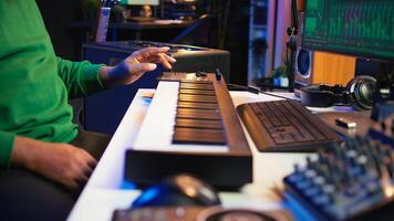 Music engineer producing song by mixing and mastering tunes on audio console, playing piano notes on synthesizer to record sounds on pc. Producer creating soundtracks with midi controller. Camera B. photo