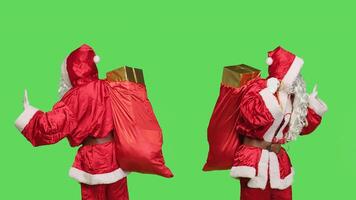 Santa claus doing push gesture in studio, having sack full of gifts against greenscreen backdrop. Man portraying father christmas on holiday, rejecting something to left or right. photo