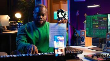 Talented composer explaining musical sheet notes during online master class recorded with smartphone in home studio. Artist musician teaching people how to read and sing accords on piano. Camera A. photo
