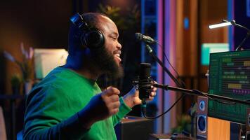 Confident songwriter performing a tune on microphone in home studio, recording his song and editing in post production. Performer artist singing aloud and using stereo equipment. Camera A. photo