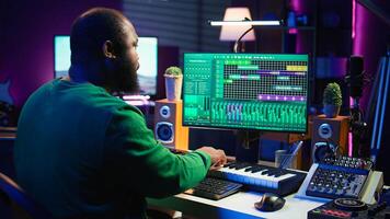 Audio engineer recording and producing new tunes on professional pc software, using mixing console and midi controller to create new music. Artist composer uses stereo gear at home studio. Camera B. photo