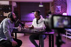 Show host and guest meeting to stream podcast episode together, creating online content with live broadcast discussion. Vlogger talking to man using professional equipment to record chat photo