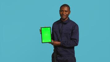 Portrait of smiling security guard at work showcasing isolated screen tablet while overseeing premises. Joyful private law enforcement worker presenting chroma key device, studio backdrop, camera B photo