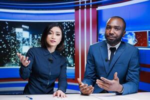 Night show hosts reviewing breaking news live on television program broadcast, working together to create interesting content for tv channel. Diverse team of journalists in newsroom. photo