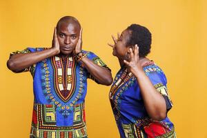 Angry african american wife shouting while husband covering ears with hands and looking at camera. Man ignoring while having argument and relationship crisis with girlfriend photo