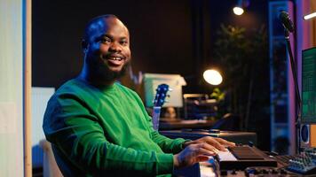 Skilled music producer creating new songs on midi controller synthesizer, working with mixing console and professional software on pc. Artist using piano and mastering acoustical tunes. Camera A. photo