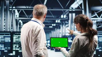 Specialists using mockup tablet to monitor energy efficient data center clusters. Server units using renewable sources employed to minimize consumption and reduce overall workplace carbon footprint photo