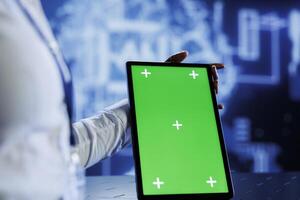 IT consultant uses green screen tablet to update neural networks, writing intricate binary code scripts on tablet. Worker uses chrome key device programming to upgrade AI simulation model photo