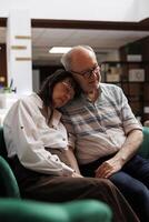 While waiting for the check-in procedure, two older couple nap on a cosy couch in a luxury lounge area. After a long travel, elderly caucasian tourists relaxes on a comfy sofa. Close-up view. photo