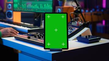 Composer editing his audio files and recordings on daw software, sitting next to a green screen display. Skilled sound technician uses mixing and mastering gear to produce new material. Camera A. photo