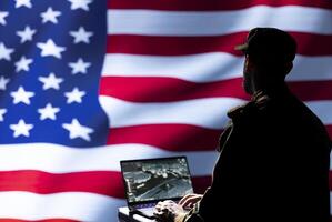 United States army specialist using target acquisition tech on laptop to detect enemy location. American patriot isolated over USA flag using satellite device to identify terrorists photo