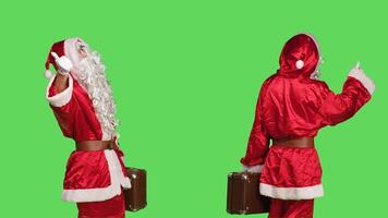 Santa claus with briefcase hitchhiking over greenscreen backdrop, asking to go somewhere while he is wearing festive costume with hat and beard. Confident man in cosplay suit with suitcase. photo