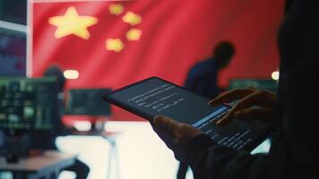 Chinese hacker uses a tablet in governmental cyber operations office to work on hybrid warfare and political manipulation. Inflicting manipulation and propaganda for the communism ideology. Camera B. photo