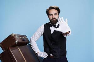 Professional doorman shows palm with gloves to express rejection over blue background, creating advertisement with refusal symbol. Bellhop showcasing his disagreement to ideas, dismissal. photo