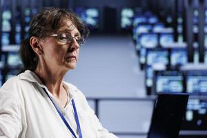 Octogenarian professional preparing server hub contingency plan monitoring data center energy consumption across components, making sure sensors are functioning flawlessly, doing routine disk checks photo