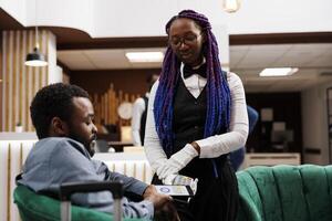 African American woman waitress giving pos machine to hotel guest waiting in lobby for check-in procedure. Tourist holding smartphone paying for order using nfc technology and banking app photo