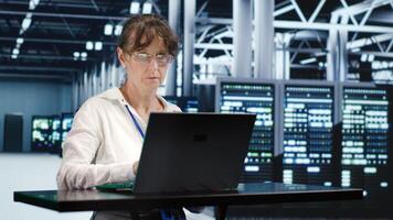 Qualified worker in server farm housing high end rows capable of quickly and efficiently performing complex computations and data analysis, using mockup laptop to get rid of problems photo