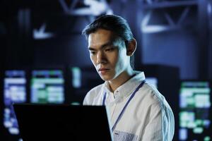 Dara center tech support running code and programming on laptop, troubleshooting and upgrading high tech facility designed to accommodate rows of fully operational server rackmounts photo