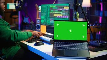 Professional artist operating on daw software in home studio, using a green screen layout next to him. Producer editing his audio recordings by applying mixing and mastering techniques. Camera B. photo