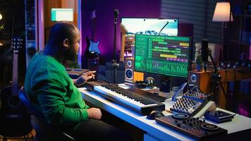 Sound engineer recording piano notes with DAW software in his home studio, working at night on producing new music with electronic tools. Musician composing tunes on midi controller. Camera B. photo