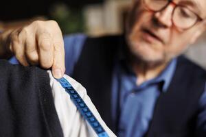 Extreme close up of blue measurement tape on elegant customer shoulder during garment fitting process. Elderly professional meticulous suitmaker honoring client sartorial comission photo