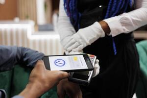 Contactless payment methods. Close up of man paying for order at hotel bar or restaurant using cellphone with nfc technology. Waiter wearing white gloves hold POS machine accept cashless transaction photo
