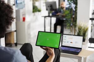 Employee holding tablet with green screen in hand in business office. Start up executive manager using digital device with chroma key display in corporate coworking space photo