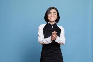 Smiling asian waitress wearing uniform applauding with to show support and appreciation portrait. Cheerful young attractive woman receptionist clapping hands and looking at camera photo