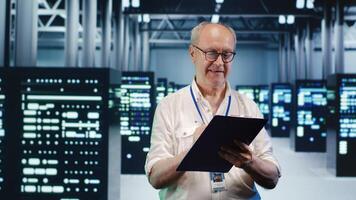 Older serviceman looking around high tech data center, using clipboard to crosscheck disaster recovery plan and assess server electronics in need of replacement, preventing errors photo