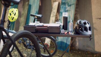 View of professional toolbox placed on table near other tools and helmet ready for bike maintenance outdoors. In yard, close-up of different specialized tools and bicycle helmet positioned on table. photo