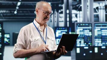 Trained IT professional navigating network of servers in industrial place. Manager with laptop ensuring perfect operations, doing optimizations and maintenance in data center photo