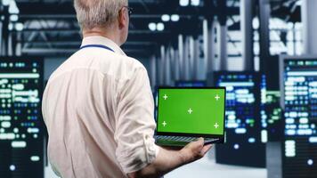 Efficient IT professional navigating network of server rigs in industrial hub. Expert using mockup laptop, ensuring proper operations, doing optimizations and maintenance in data center photo