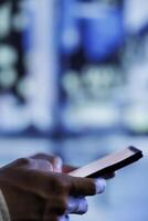 Man having fun walking around city at night, scrolling on social media using mobile phone, close up. Citizen using smartphone while wandering on empty town blurry background photo